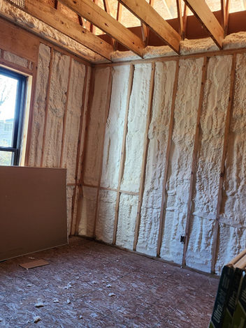 Unfinished room showing spray foam insulation on walls, wood framing, window.