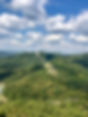 Lush green forested mountains under a blue cloudy sky