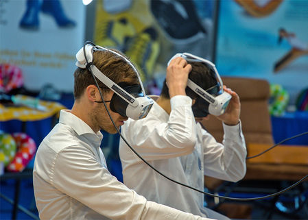 Zwei Personen tragen Virtual-Reality-Headsets und sitzen nebeneinander an einem Tisch