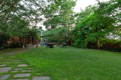 Large green lawn with stone path, lush trees, and distant house.