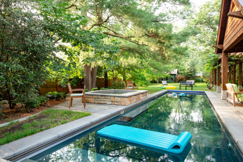 Modern swimming pool with blue float, stone fire pit, lush backyard.