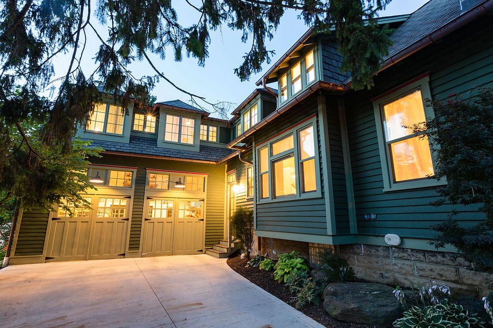 Green house at dusk with illuminated windows and garage doors