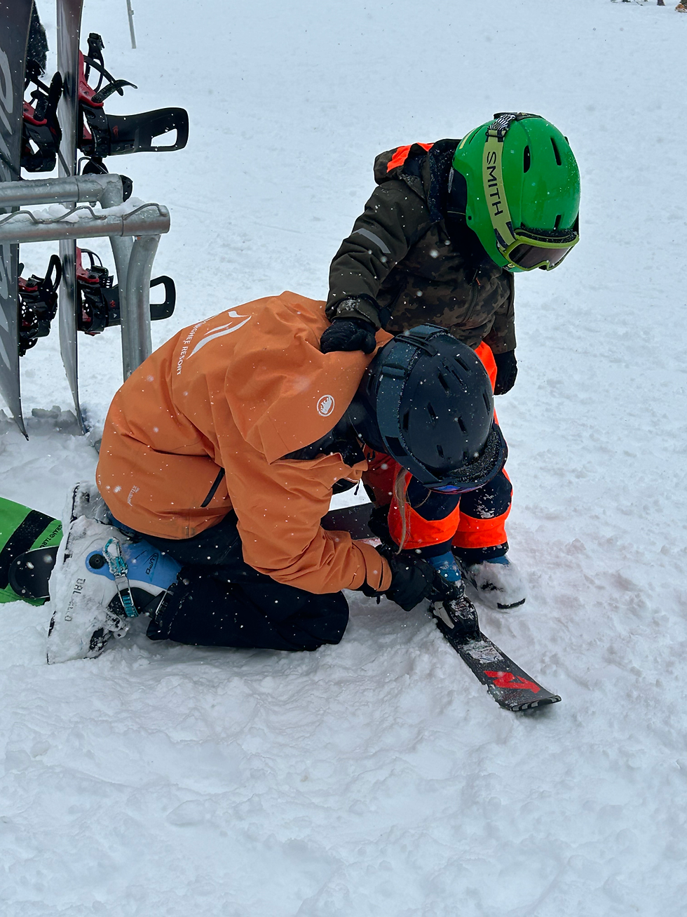 Maeve helping a little one put his skis on