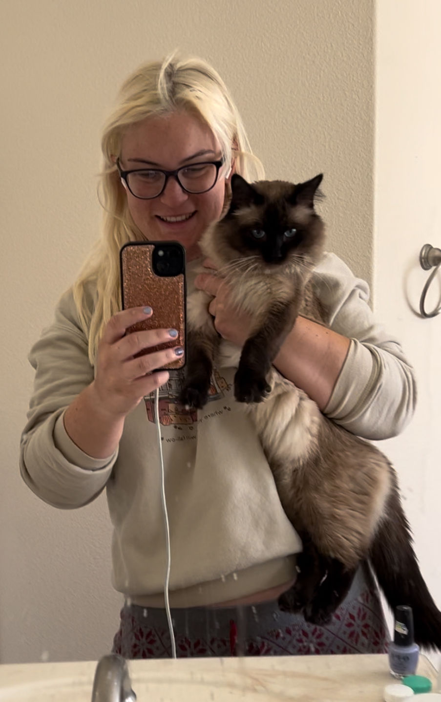 A woman holding a ragdoll cat, taking a mirror picture.