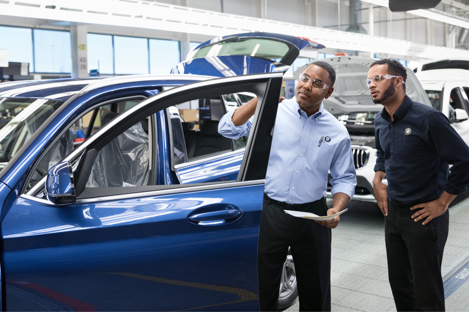 Zwei BMW Techniker in der Produktion der Automobilindustrie kontrollieren die Tür eines blauen BMW Autos in der Endabnahme.