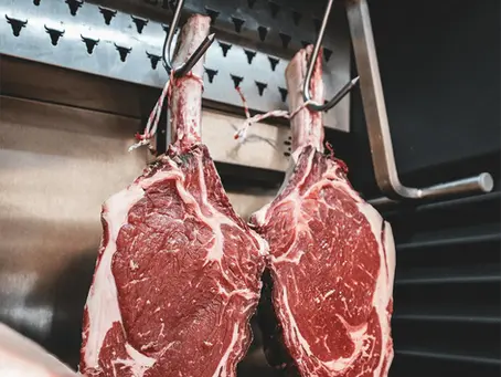 Two legs of beef hanging from metal hooks in a clean butchery.