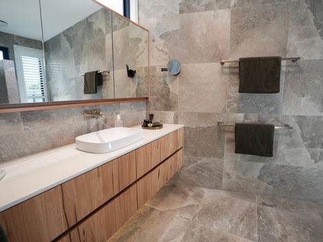 This contemporary custom residence has been meticulously designed to maximise its street
presence and deliver an impactful first impression. Drawing inspiration from the surrounding
native bushland, the interior colour scheme incorporates natural tones to inherit a sense of
harmony and environmental connection.
Natural granite is a prominent material throughout the property, featured in the kitchen
island, rangehood, and powder room splashbacks. The granite also envelops the fireplace,
establishing a dramatic focal point visible from the entrance hallway.
‘Rock Salt’ stone-inspired porcelain tiles, specified for both floors and walls in all wet areas,
evoke a luxurious day-spa ambience. These large-format 1200x1200 tiles extend seamlessly
from the façade and portico ‘spine wall’ into the front entrance and formal lounge, ensuring
visual continuity and a smooth transition between the exterior and interior.
Warm vinyl flooring paired with natural timber elements, complemented by green and tan
accents, contributes to a welcoming and cohesive atmosphere throughout. The selection
and coordination of furniture, lighting, artwork, mirrors, window furnishings, linen, and décor
were carefully curated to achieve a unified interior aesthetic.
The entire build process was guided by close collaboration with my clients, who entrusted
my expertise throughout the entire building journey. This resulted in creating a beautiful
home to enjoy, cherish, and proudly call their own.