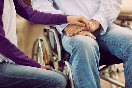 Man in a wheelchair with their carer holding their hand