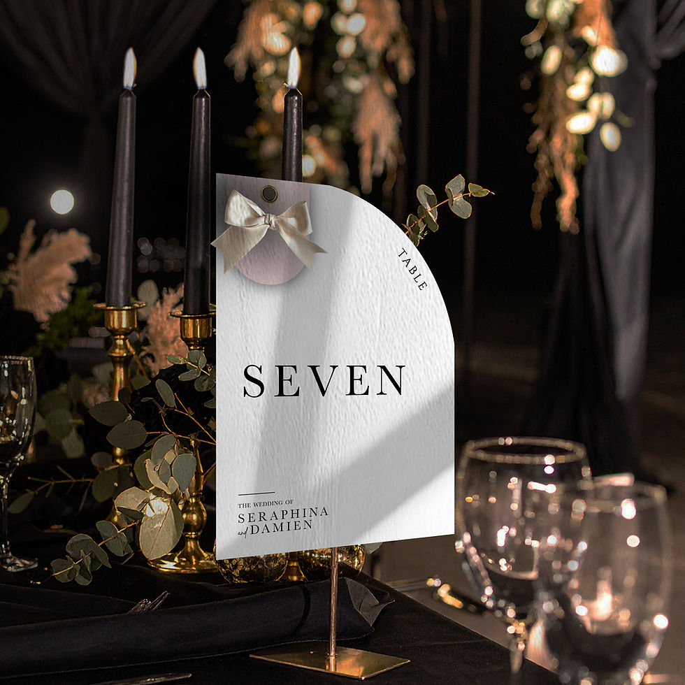 Minimalist arched wedding table number with black typography and ribbon detail on a candlelit black table setting