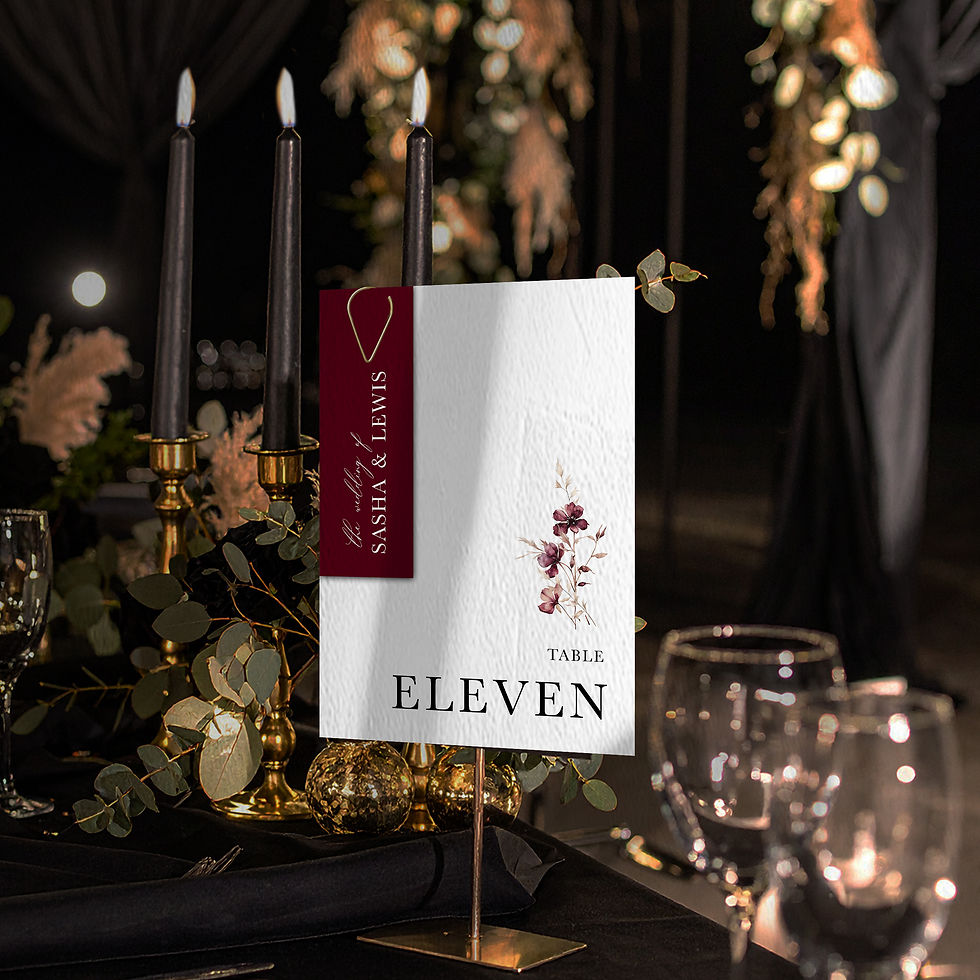 Wedding table number with burgundy tag detail, styled on a black table with candlelight, gold accents and foliage.