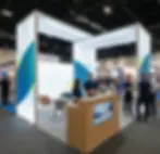 Ein individuell gestalteter, beleuchteter Messestand auf einer Fachmesse mit modernem Infocounter, Sitzlounge und Beratungspersonal im Gespräch.