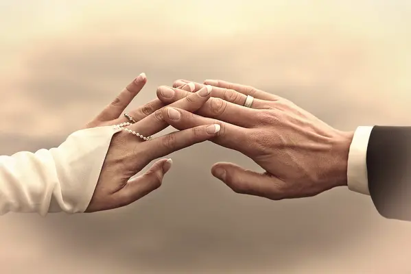 Hände von Braut und Bräutigam ineinander verschränkt vor wolkigem Himmel