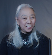 A headshot of Yasuko Tokunaga from interview with grey background in Philadelphia.