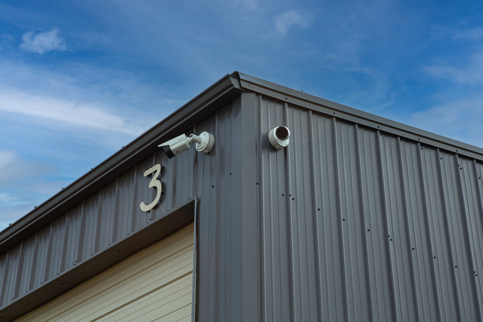 The corner of a grey storage building with two security cameras on it.