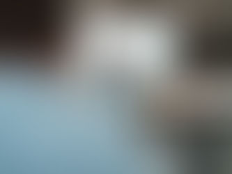 Woman in blue sweater presenting in an office with graphs on a screen. She holds a tablet, and colleagues are seated at a white table.