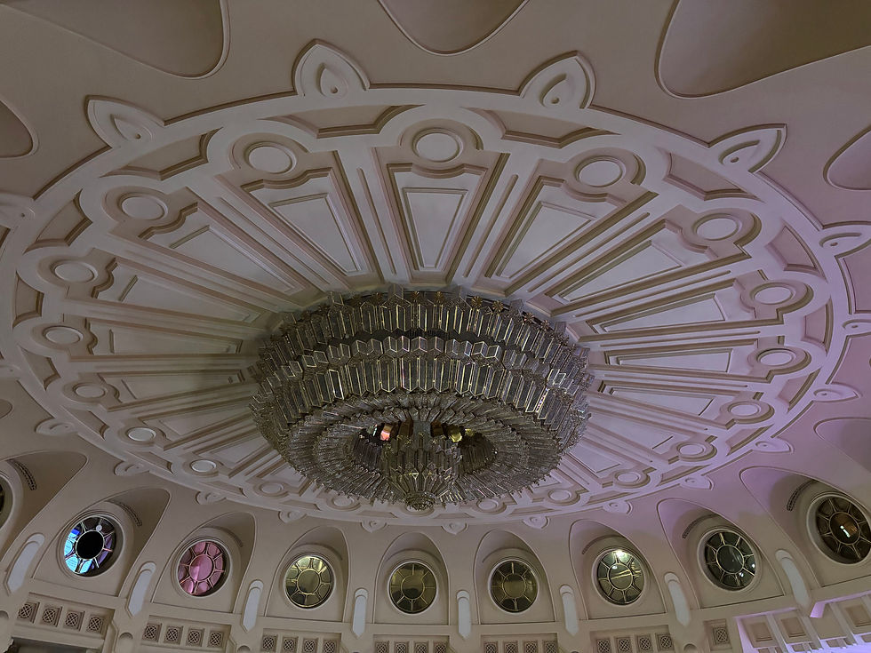 Ornate ceiling with a large, detailed chandelier in a dome. Circular windows with stained glass in blue, pink, and gold hues add color.