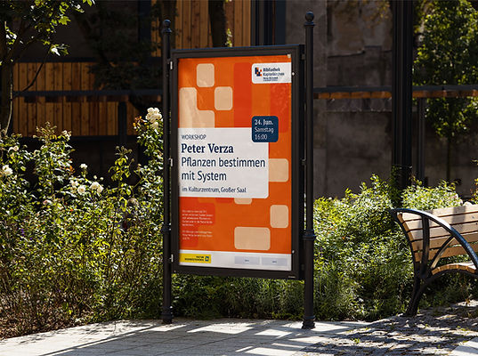 Photomontage von eienm Plakatständer mit einem grafischen Veranstaltungspalkat. Im Hintergrund des Plakats sind die Code-Zeichen als dekoratives Element genutzt