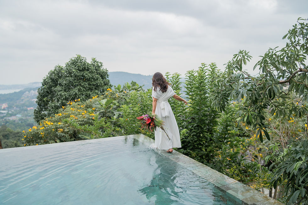 bride in a white dress balances on the edge of an infinity pool, holding tropical flowers. Lush greenery and thailand hills fill the serene background Panacea Retreat Villa in koh samui island in Thailand