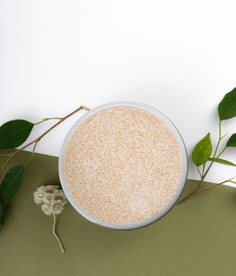 Gros plan de la texture crémeuse et exfoliante de l’exfoliant corporel O’terra dans un pot ouvert.
