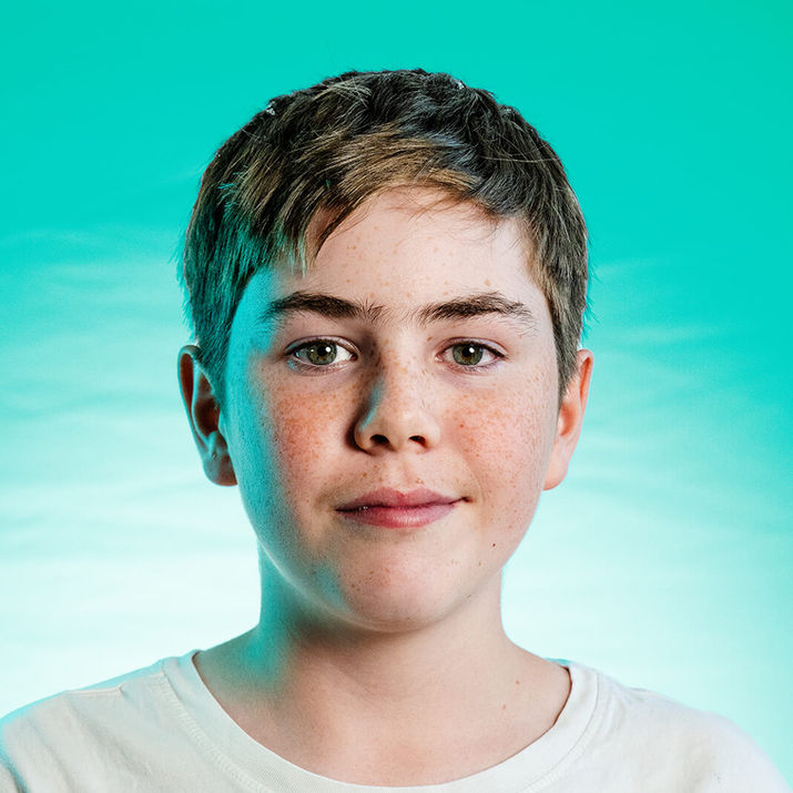Portrait d’adolescent aux cheveux courts sur fond turquoise.