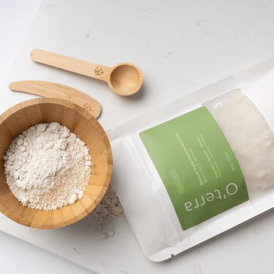 Poudre de masque à l’argile blanche O’terra dans un bol en bois avec accessoires de soin naturels.