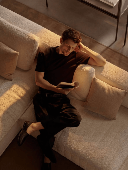 Homme lisant un livre sur un canapé blanc éclairé par le soleil.