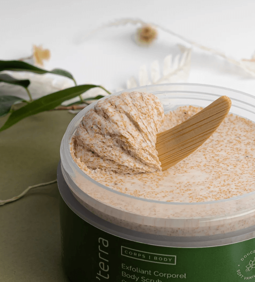 Exfoliant corporel O’terra avec texture fouettée et spatule en bois dans un décor naturel minimaliste.