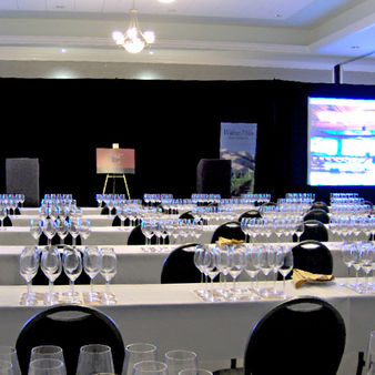 Wine glasses arranged on tables in hotel meeting room for professional conference with meeting AV projector screens.