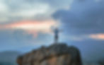 man standing on rock with arms outstretched with expansive sky in background