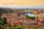 Aerial view of Florence, Italy, with terracotta rooftops, the Arno River, and Ponte Vecchio under a warm, orange sky.