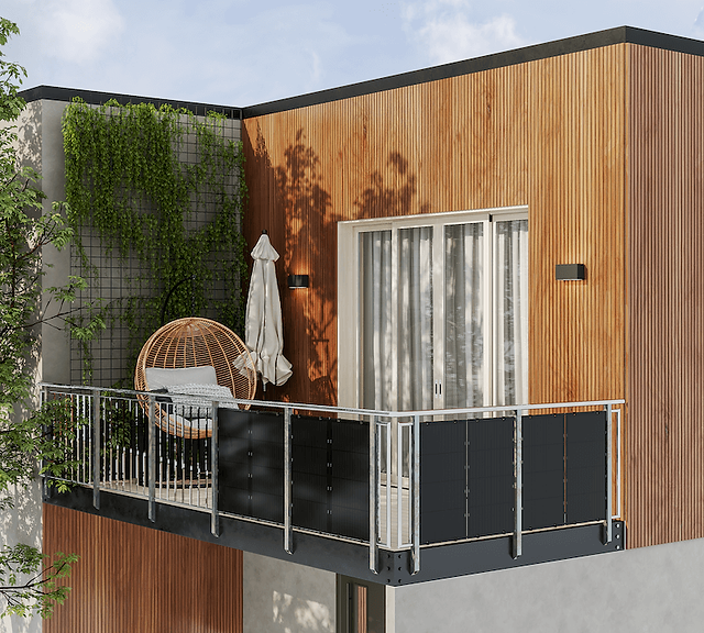 Zdjęcie przedstawia nowoczesny balkon przy drewnianej elewacji budynku. Balustrada balkonu wykonana jest z metalowych poręczy oraz zamontowanych ciemnych paneli fotowoltaicznych. Na balkonie znajduje się okrągły wiszący fotel z rattanu, wyłożony poduszkami, oraz stojący w rogu złożony parasol ogrodowy. Ściana budynku z lewej strony pokryta jest pnącymi roślinami, co dodaje naturalnego akcentu do przestrzeni. Balkon sąsiaduje z dużymi, przeszklonymi drzwiami, przez które widać zasłony wewnątrz pomieszczenia. Jasne drewno elewacji i zielona roślinność tworzą harmonijną, spokojną atmosferę.