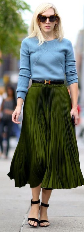 Mulher loira andando na rua e vestindo look com suéter azul bebê e saia verde.