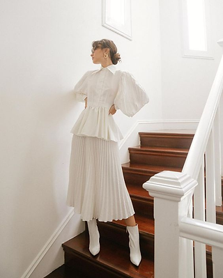 Modelo usa look branco com blusa peplum e saia plissada