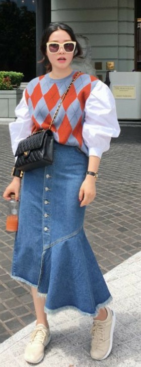 Modelo asiática veste saia jeans assimétrica com suéter xadrez e bolsa chanel preta.