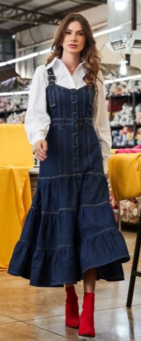 Modelo de cabelo solto usando vestido de alça jeans midi, com camisa branca e bota vermelha.