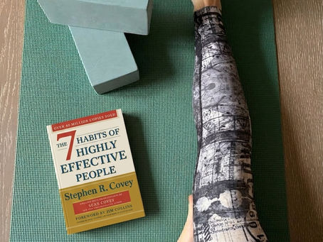 A photo of the author sitting in a yoga pose, with two yoga blocks and a copy of the 7 habits of highly effective people on the yoga mat