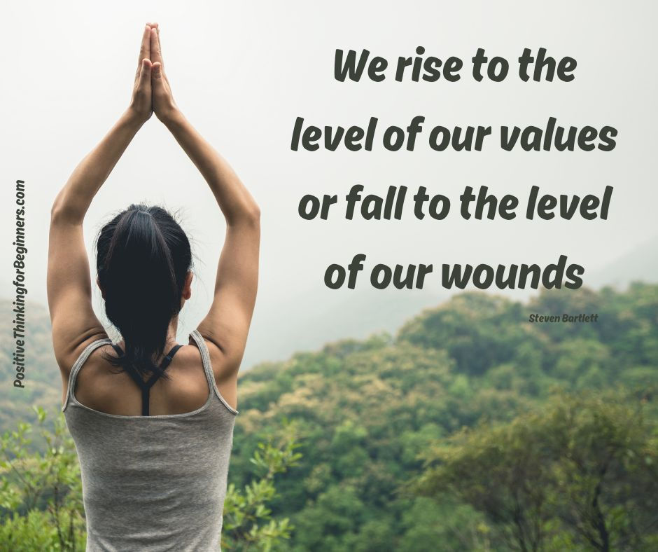 Woman in gray tank top doing yoga with hands in prayer pose, overlooking lush green hills. Text reads "We rise to the level of our values or fall to the level of our wounds."