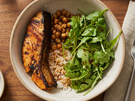 A bowl of rice with salmon, chickpeas, and arugula in a rustic, elegant setting