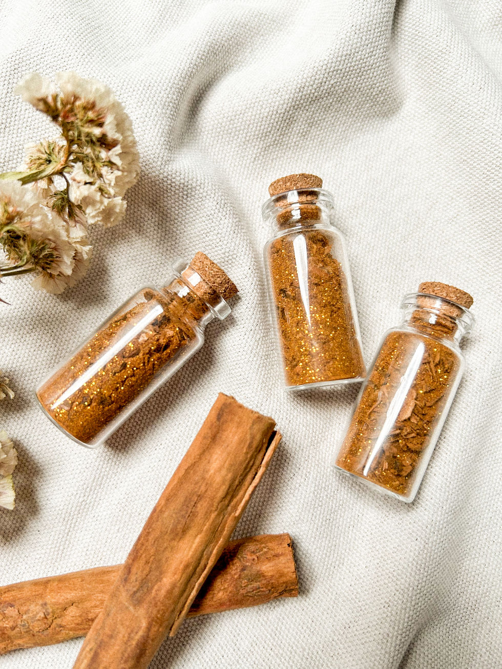 Imagen cenital de tres frascos de vidrio con tapadera de corcho con mezcla de canela y otras hierbas adentro