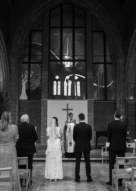 - Bride and groom standing before the officiant at the altar, hands joined under stained-glass windows.