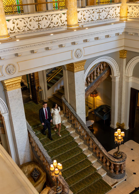 - Bride and groom smiling as they descend a sweeping marble staircase under warm chandelier light.
