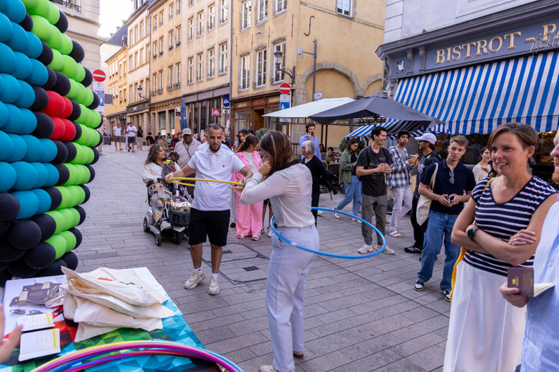 A woman hula hoops in front of a balloon arch while people gather around during a lively street festival.