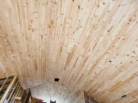 Techo abovedado revestido con tablas de madera clara sobre la estructura de madera vista de la pared.