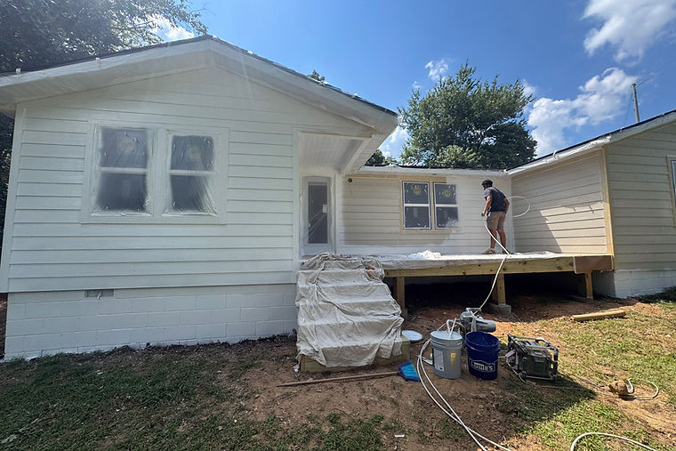 Exterior painting in progress with masked windows and protective covers.