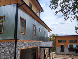 Fachada lateral con revestimiento metálico, detalles de madera y obras en curso a nivel del suelo.