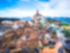 Amusement park with a snowy mountain ride, colorful tracks, and a winding road. Visitors walk below a blue sky, creating a lively scene.