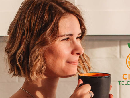 Woman in a white top enjoying a drink from a black mug in a bright kitchen. "Citrus Telemedicine" logo visible. Warm, relaxed mood.