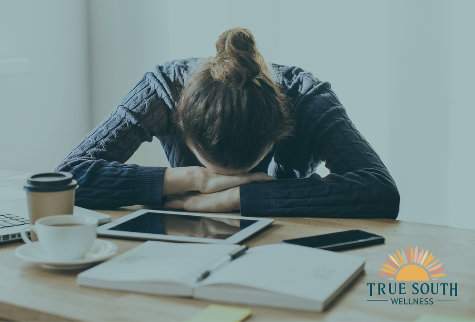 Person with head down on desk, surrounded by a tablet, phone, and coffee. Weariness. Logo: True South Wellness. Bright, soft-lit room.