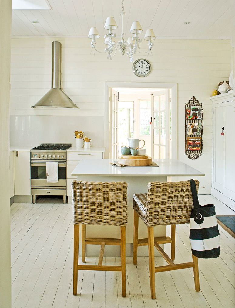 Breezy Australian beach house kitchen with island, woven stools, white painted floorboards and white chandelier