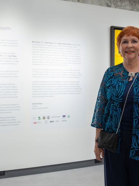 Adlín Ríos Rigau posa junto al texto curatorial de la exposición ELLAS, maestras del arte puertorriqueño, en la renovada Sala FAR.